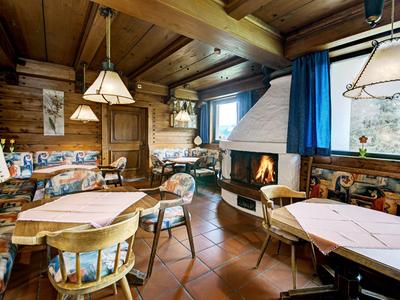 Rustikaler Gastraum mit Holzbalkendecke, Kamin und Tischen mit Stühlen.