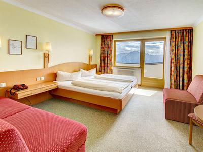 Helles Hotelzimmer mit Doppelbett, Sofa, Tisch, Nachttischlampen und Balkon mit Bergblick.
