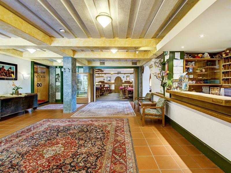 Großer Rezeptionsbereich mit hölzernen Balken, Teppichen, Theke und Bücherregalen an der Wand.