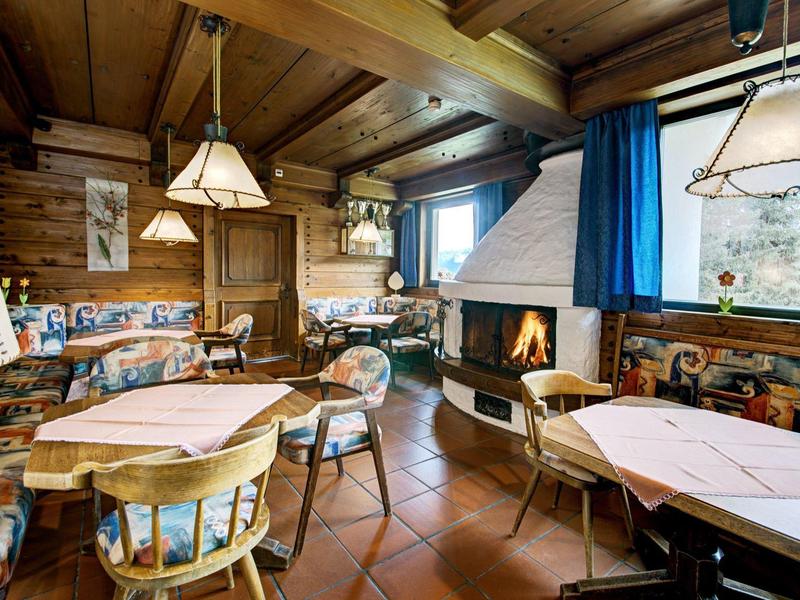 Gemütlicher Holzraum mit Tischen, Stühlen, Kamin und blauen Vorhängen, rustikales Ambiente.