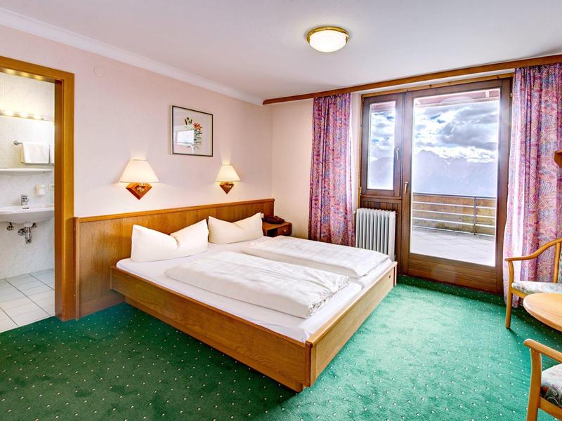 Gemütliches Hotelzimmer mit Doppelbett, grünem Teppich, Balkon und angrenzendem Badezimmer.