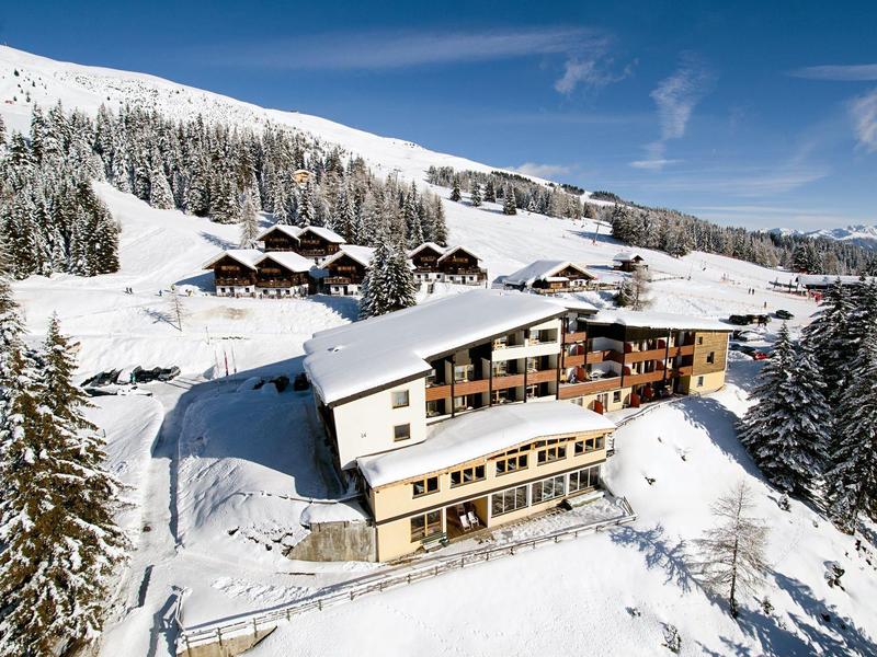 Verschneite Berglandschaft mit großen Chalets aus Holz und blauem Himmel im Hintergrund.