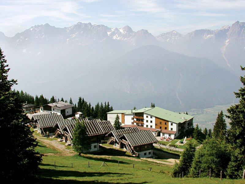 Bergdorf mit Holzhäusern und Tannen, im Hintergrund hohe Nebel-umhüllte Berge.