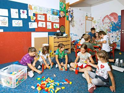 Kinder sitzen auf blauem Teppich und bauen mit bunten Bausteinen in einem farbenfrohen Raum.