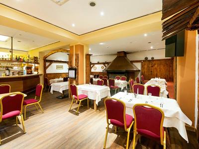 Gemütlicher Hotelrestaurantbereich mit weißen Tischtüchern, roten Stühlen und einer rustikalen Holzdecke.