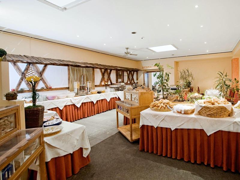 Großer, hell beleuchteter Frühstücksraum mit gedeckten Tischen und Buffet mit Backwaren und Pflanzen.