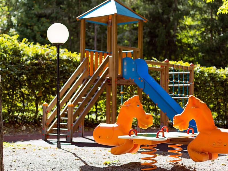 Bunter Kinderspielplatz mit Rutsche, Klettergerüst und Wipptier im Waldpark.