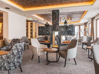 Modern eingerichteter Hotel-Loungebereich mit gemütlichen Sesseln, Tischen und indirekter Beleuchtung.