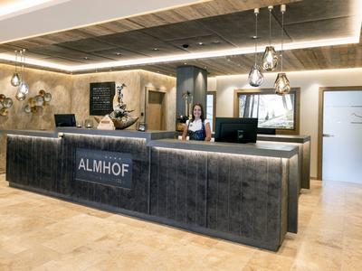 Moderner Empfangsbereich mit hellem Boden, dunkler Theke und warmem Licht, dekorativer Wildholzwand.