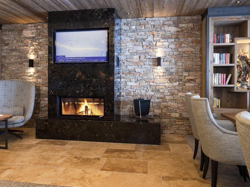 Gezellige hotellounge met open haard, stenen muur, fauteuils en boekenkast.