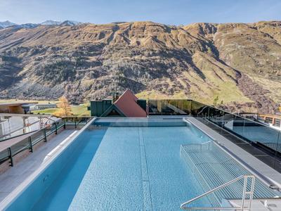 A clear rooftop pool overlooking mountainous landscape under clear weather.
