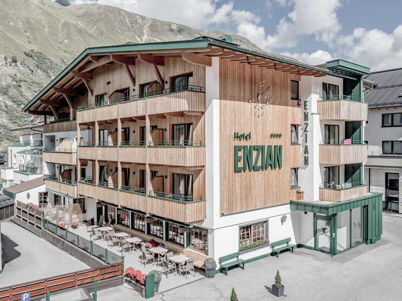 Multi-story alpine-style hotel with balconies and surrounding mountains under clear sky.