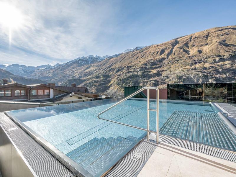 Modern outdoor pool with glass railing and mountain view under sunshine.