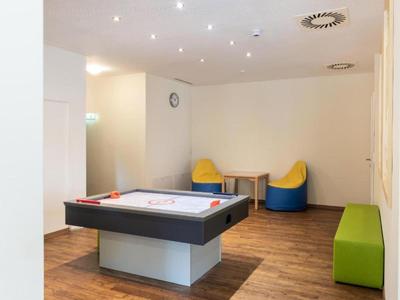Game room with air hockey table, colorful bean bags, and green bench on wooden floor.