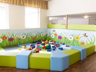 Bunter Kinderspielbereich mit Bausteinen und gepolsterten Sitzflächen vor bemalter Wand mit Blumen.