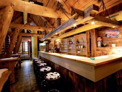 Gemütliche Holztaverne mit rustikalem Tresen, Kuhfell-Hockern und warmem Licht.