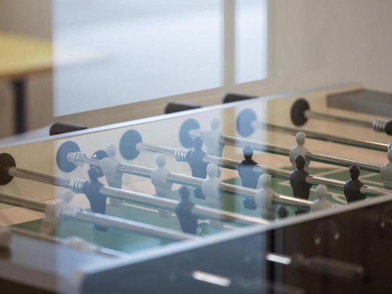 Ein Tischkicker mit schwarzen und weißen Spielfiguren hinter einer Glasscheibe in hellem Raum.