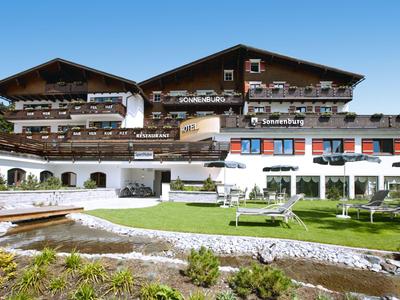 Großes traditionelles Hotel mit Holzfassade, Balkonblumen und Liegestühlen auf grünem Rasen.