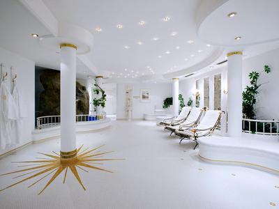 Espace bien-être lumineux avec chaises longues blanches, colonnes et plantes au design moderne.