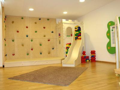 Sala de juegos infantil luminosa con pared para escalar, tobogán y suelo de madera.