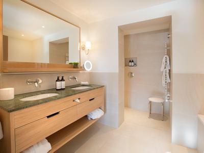 Baño luminoso con tocador de madera, espejo grande y ducha a ras de suelo con taburete.