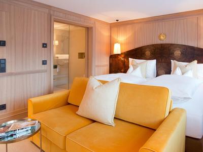 Habitación de hotel moderna con sofá amarillo, cama doble y paneles de madera en la pared.