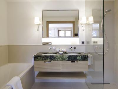 Baño moderno con bañera, doble lavabo y ducha walk-in tras mampara de vidrio.