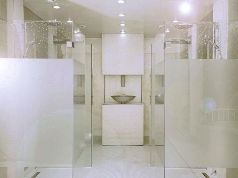 Baño moderno con paredes claras, paneles de vidrio y diseño minimalista.