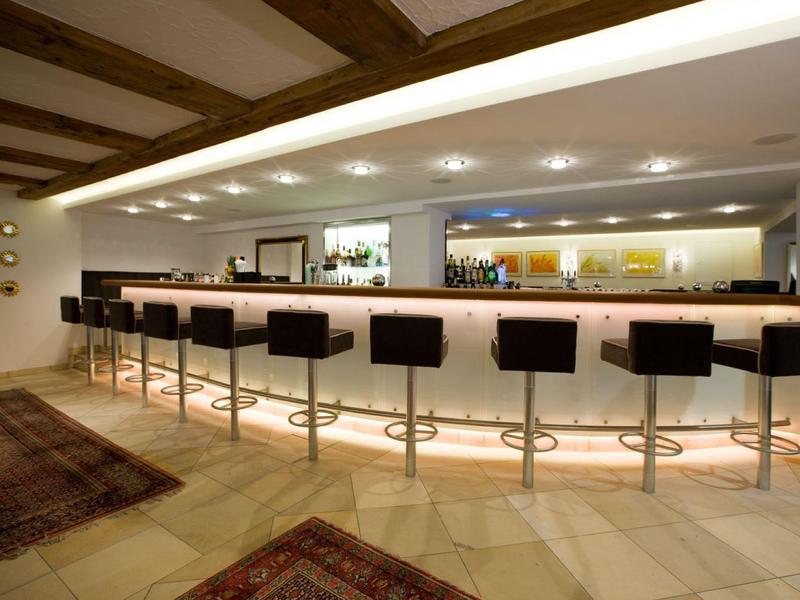 Área de bar moderna en hotel con taburetes negros e iluminación indirecta bajo la barra