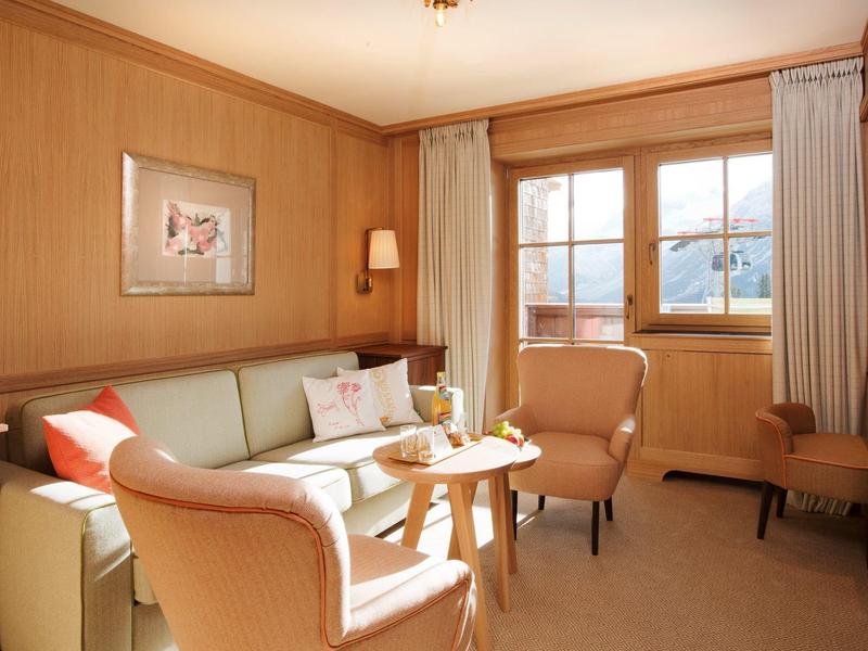 Acogedora zona de estar en habitación de hotel con sofá, sillones, paredes de madera y vista a las montañas.