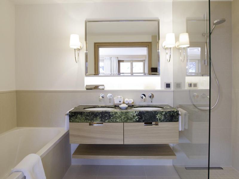 Baño moderno con bañera, doble lavabo y ducha walk-in tras mampara de vidrio.