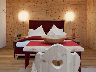 Gemütliches Schlafzimmer mit Holzwänden und -boden, rotem Bett und Herz-Stuhl.