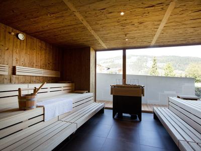 Helle Sauna mit hellen Holzliegen, hölzernem Eimer und großen Fenster mit Bergblick.