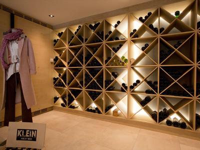 Cave à vin avec étagère en bois éclairée et mannequin portant un manteau et une écharpe.