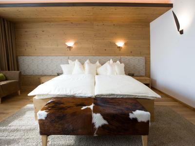 Gemütliches Schlafzimmer mit Holzwänden, Doppelbett, weißen Kissen und braun-weißem Hocker.