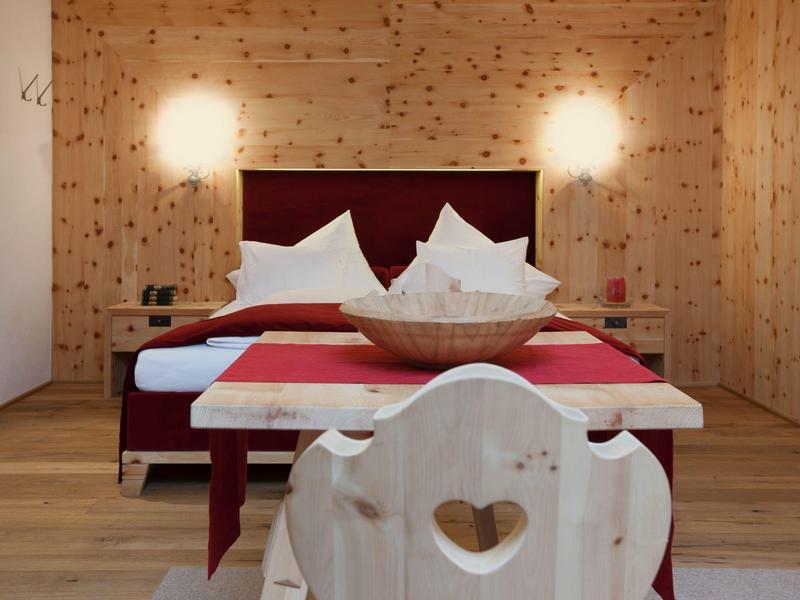 Gemütliches Schlafzimmer mit Holzwänden und -boden, rotem Bett und Herz-Stuhl.