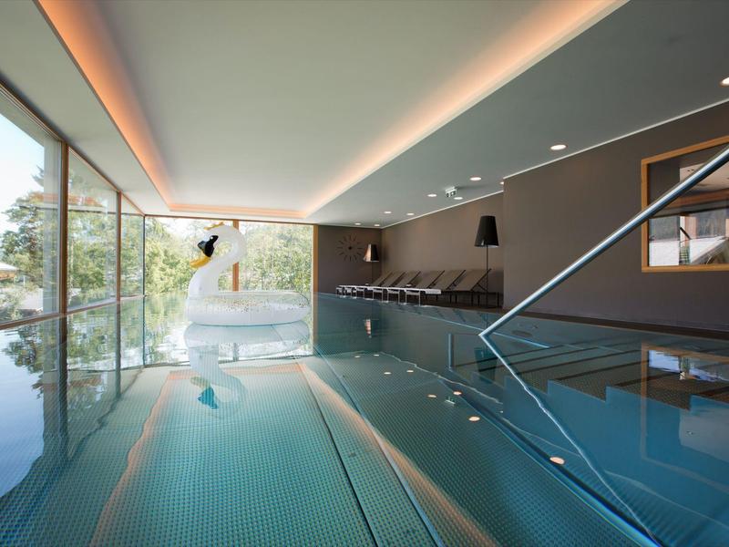 Moderner Innenpool mit großen Glasfenstern, Holzdecke und ruhiger Wasserfläche.