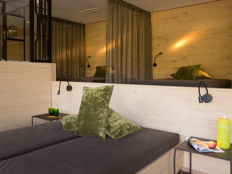 Gemütliche Zimmerecke mit grauem Sofa, grünen Kissen, Holzwänden und Nebenbeleuchtung.