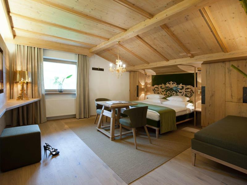 Gemütliches Schlafzimmer mit Holzwänden, Doppelbett, Stühlen, Fenster und weichem Teppich.