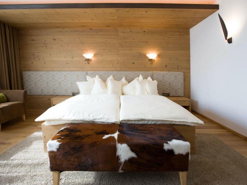 Gemütliches Schlafzimmer mit Holzwänden, Doppelbett, weißen Kissen und braun-weißem Hocker.