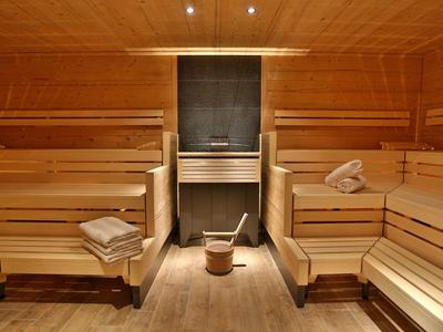 Innensauna aus hellem Holz mit Holzbänken, Eimer und Schöpflöffel, Handtücher liegen bereit.