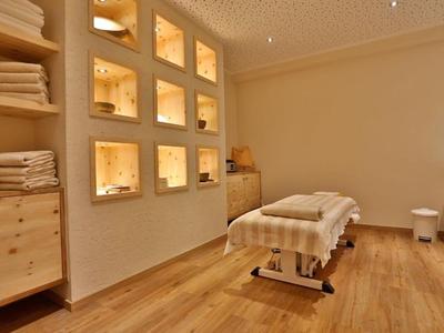 Warmer Massageraum mit Holzboden, beleuchteten Wandnischen, Handtüchern und Massageliege.