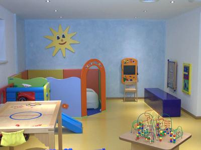 Kinderspielzimmer mit buntem Spielzeug, Rutsche, Spieltisch und Wanddekoration mit lachender Sonne.