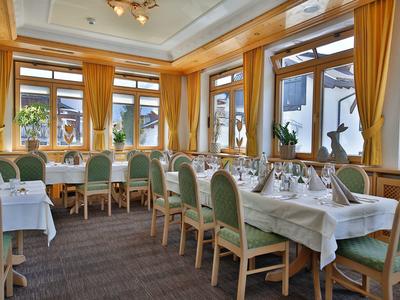 Helles Restaurant mit Holzakzenten, grünen Stühlen und weiß gedeckten Tischen, sonnendurchflutet.