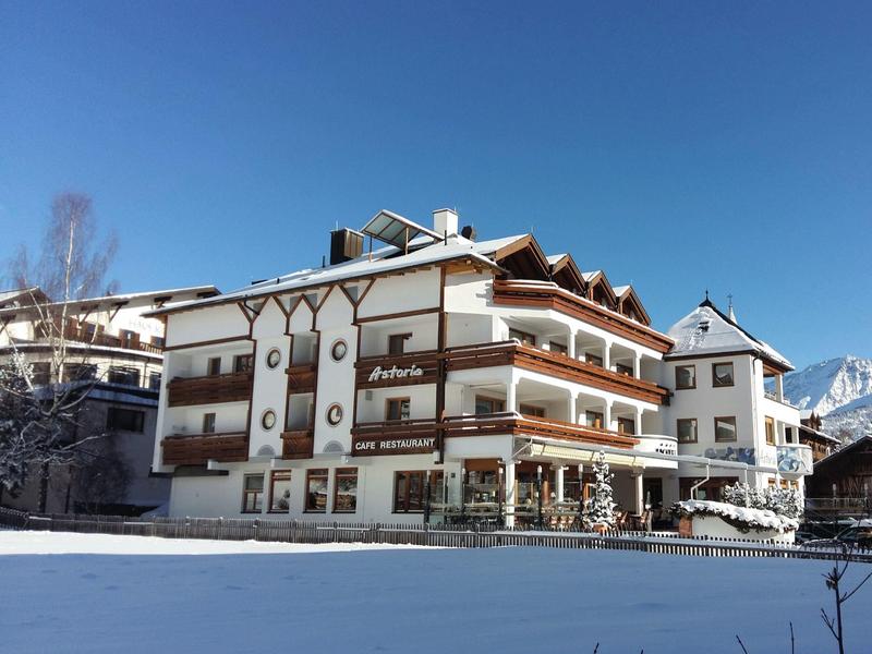 Großes Hotelgebäude im alpinen Stil mit Balkonen bei klarem Himmel und Bergkulisse.