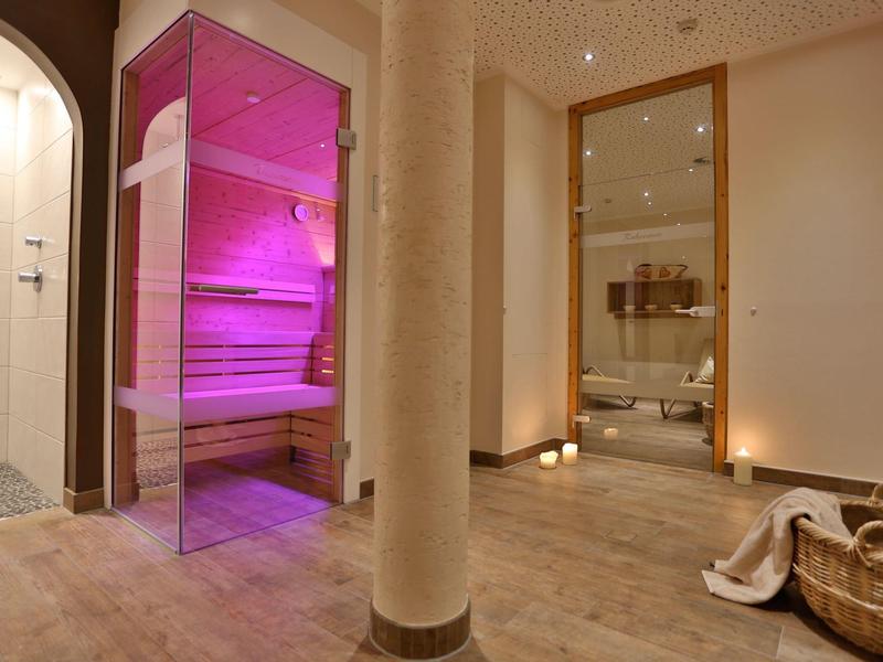 Moderner Wellnessraum mit pink beleuchteter Sauna, hellem Holzfußboden und entspannter Atmosphäre.