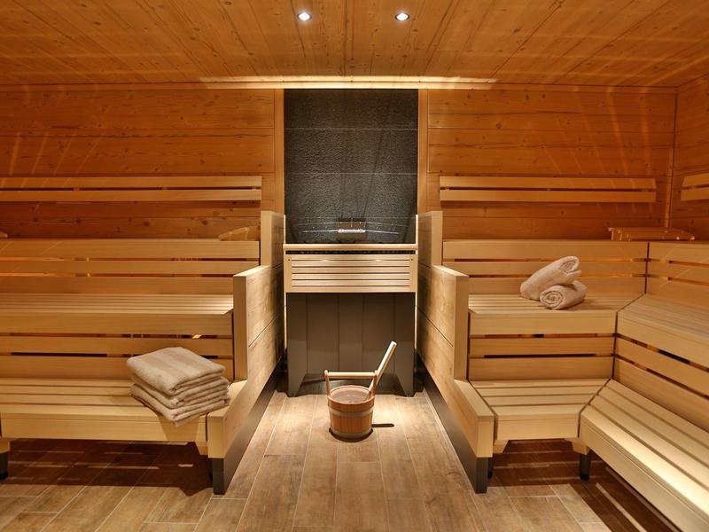 Innensauna aus hellem Holz mit Holzbänken, Eimer und Schöpflöffel, Handtücher liegen bereit.