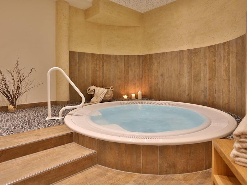 Runder Whirlpool mit Stufen, Kerzen und Holzwand in einem ruhigen Spa-Bereich.