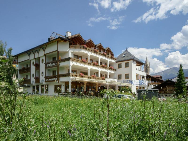 Mehrstöckiges Hotelgebäude mit Holzbalkonen vor grünem Feld und blauem Himmel