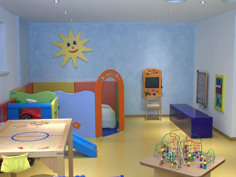 Kinderspielzimmer mit buntem Spielzeug, Rutsche, Spieltisch und Wanddekoration mit lachender Sonne.